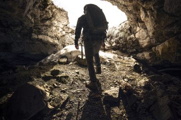 A caver with a pack walking towards the entrance of a Black Hills Cave