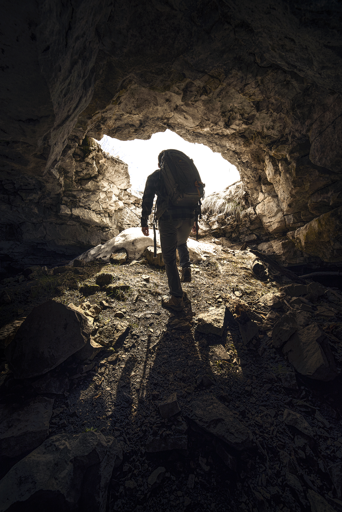 A caver with a pack walking towards the entrance of a Black Hills Cave